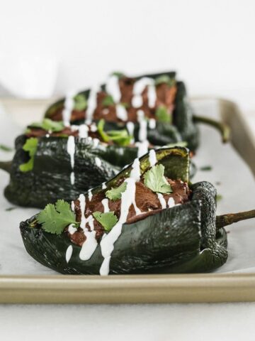 Mole chicken stuffed poblanos topped with cilantro and a white sauce on a baking sheet.