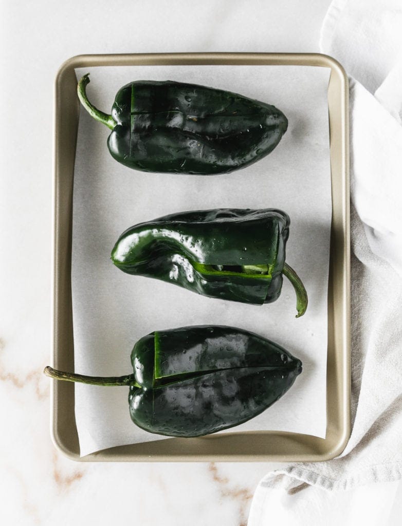 Poblano peppers cut open ready to be stuffed with chicken mole on a baking sheet.