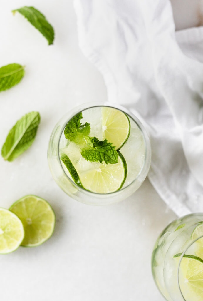 overhead view of a white wine mojito in a wine glass with fresh mint and limes around it.