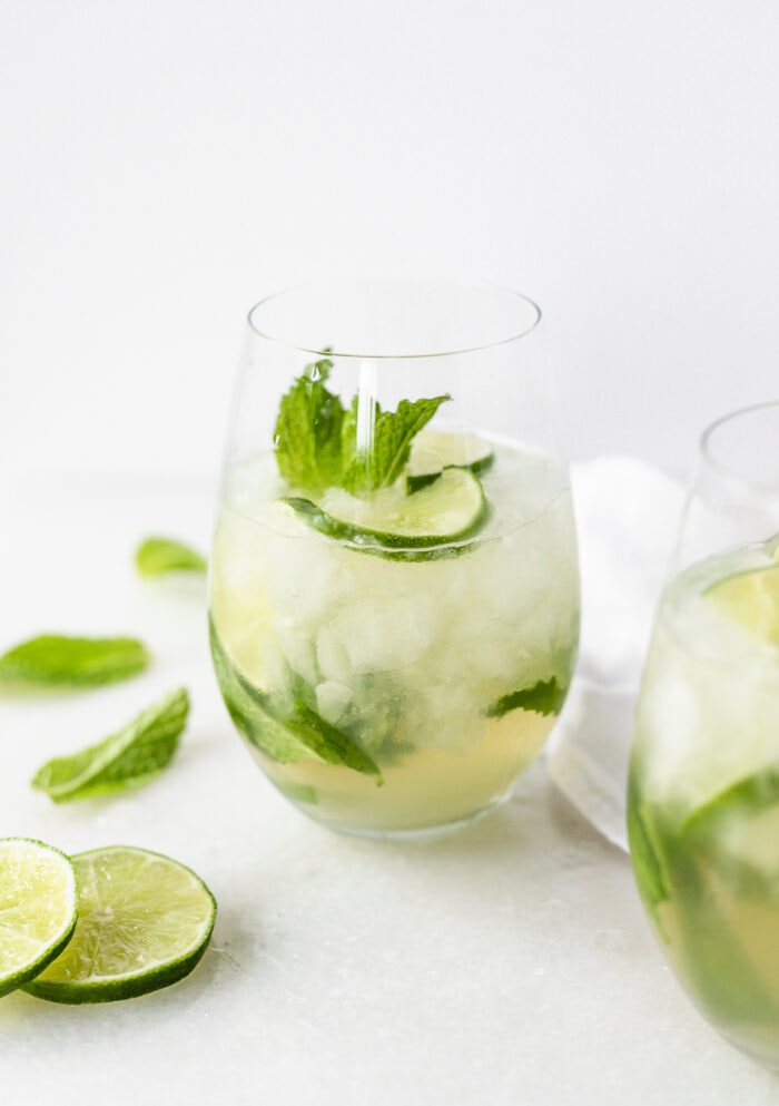 white wine mojito in a stemless wine glass with lime slices and mint around it.