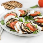 grilled eggplant, tomato and mozarella caprese salad on a grey plate with grilled toast in the background.
