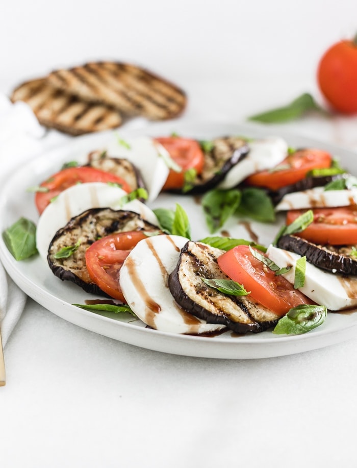 grilled eggplant, tomato and mozarella caprese salad on a grey plate with grilled toast in the background