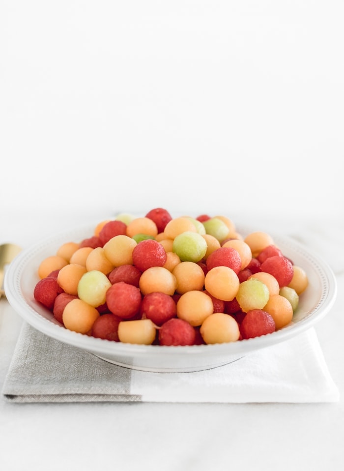 melon balls in a white bowl on top of a grey and white napkin.