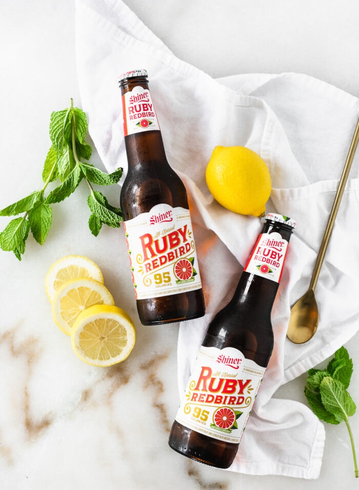 overhead view of ruby redbird beer bottles with lemons, mint, and a cocktail spoon.