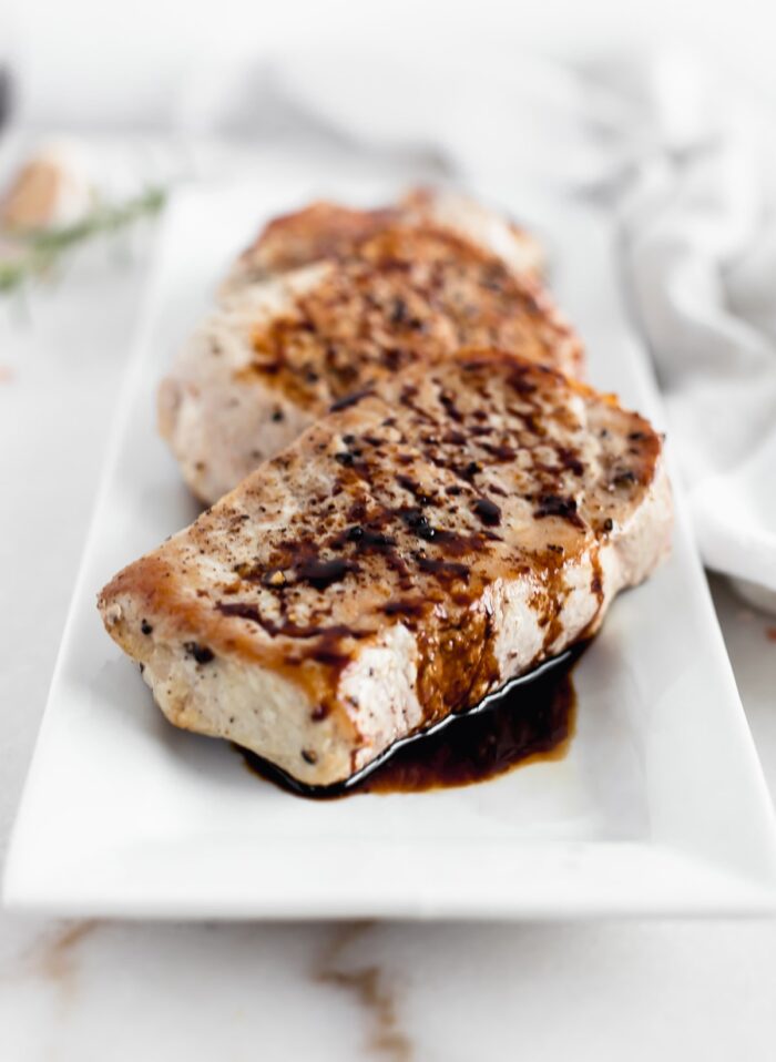 closeup of balsamic skillet pork chops on a white rectangular platter.