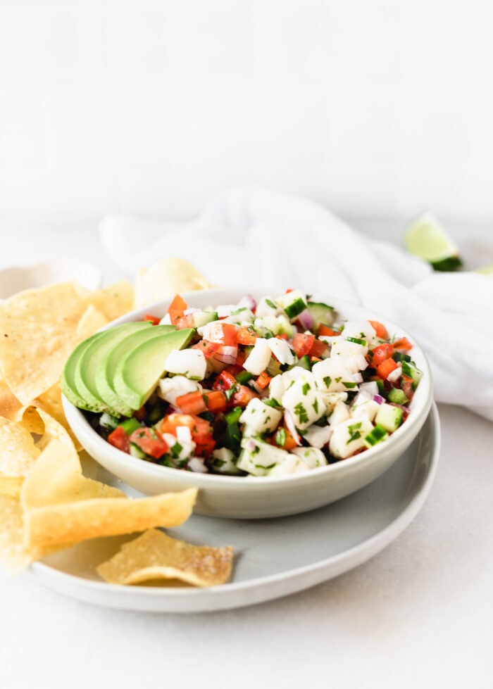bowl of ceviche with sliced avocado on top on a plate with tortilla chips.
