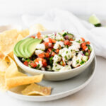 bowl of ceviche with sliced avocado on top on a plate with tortilla chips.