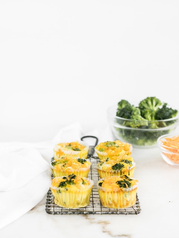 Broccoli Cheddar Egg Muffins on a wire cooling rack with a bowl of broccoli and a bowl of cheese in the background.