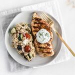 overhead view of Healthy Greek Chicken with Tzatziki Sauce on a plate with greek orzo salad and a gold fork.