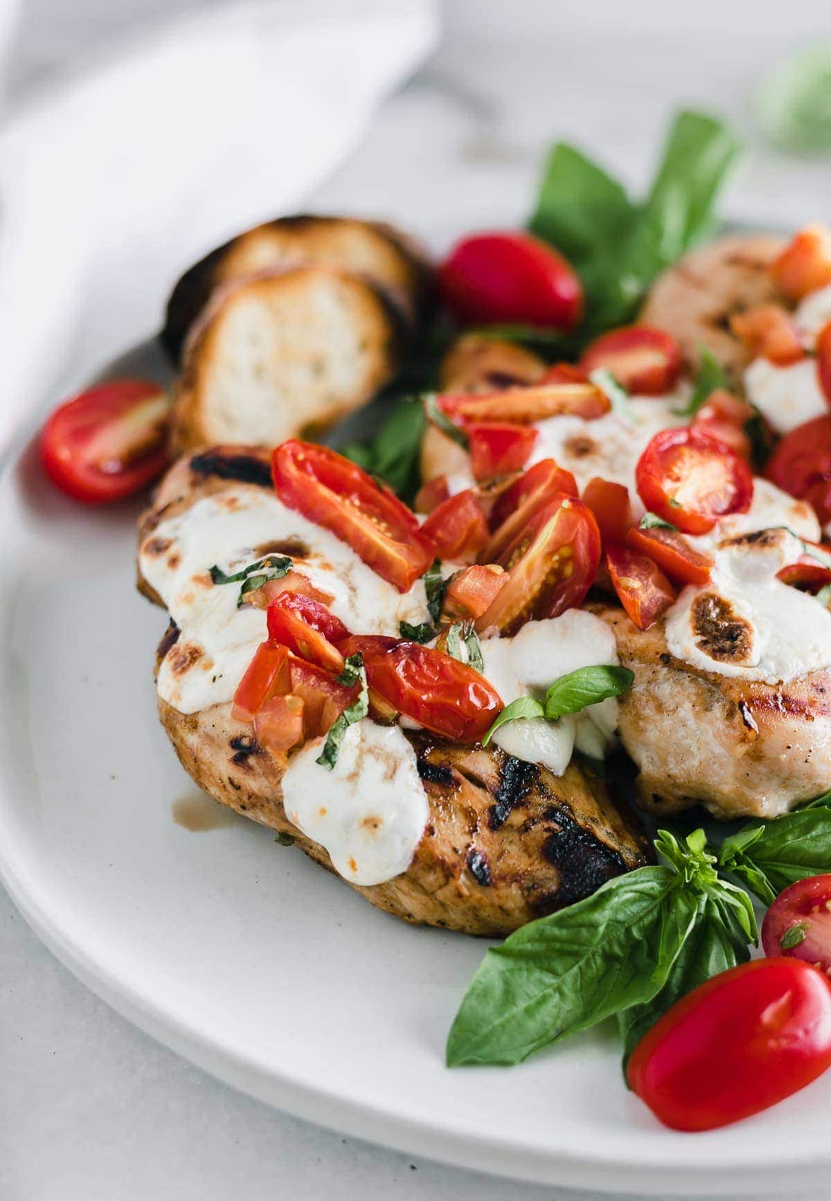 3 Tomato basil bruschetta Chicken breasts on a round cutting board with basil leaves.