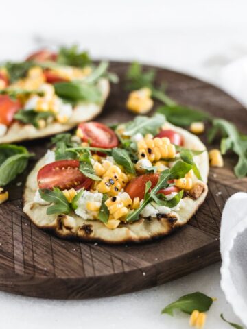 closeup view of grilled corn and goat cheese flatbread on a wooden serving board.