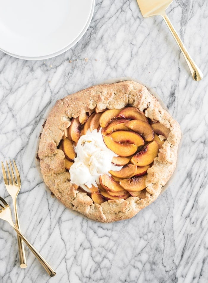 overhead view of peach galette with ice cream on top on a marble backdrop