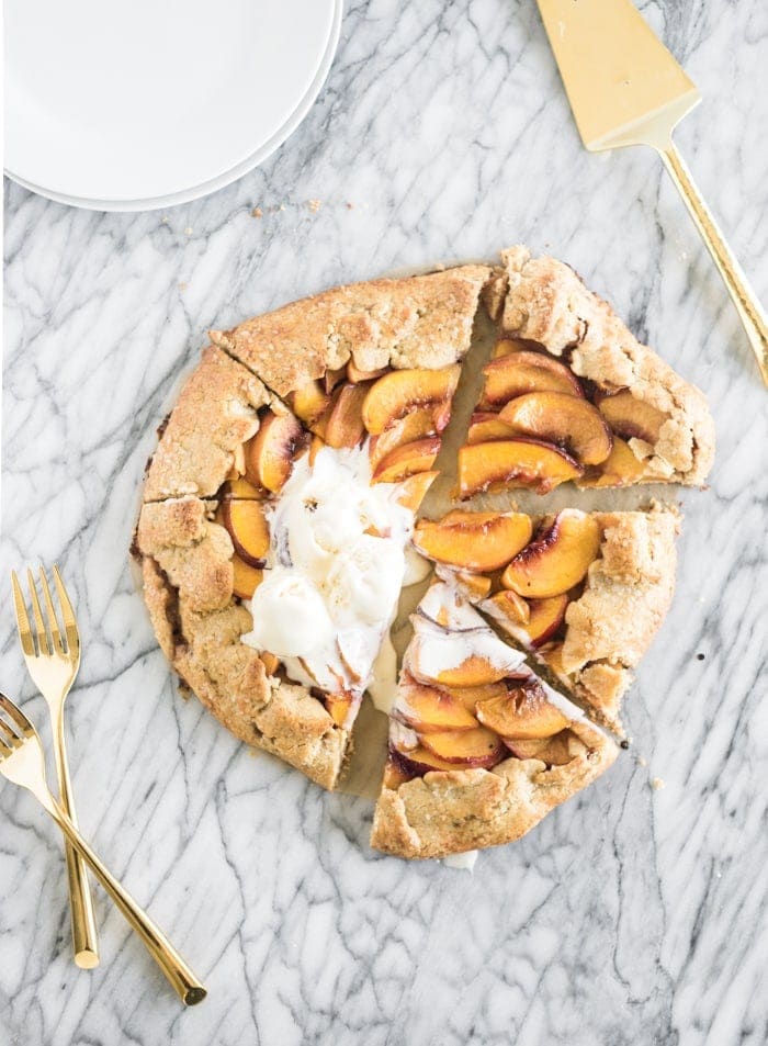 overhead view of a sliced whole wheat peach galette with ice cream on top on a marble background.