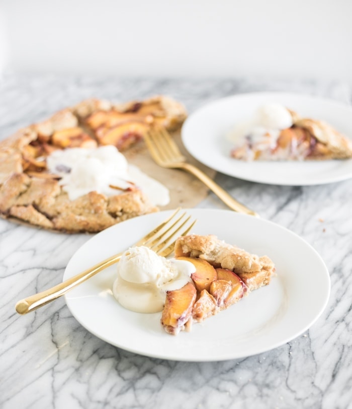 whole wheat peach galette slice on a white plate with a gold fork and a scoop of ice cream.