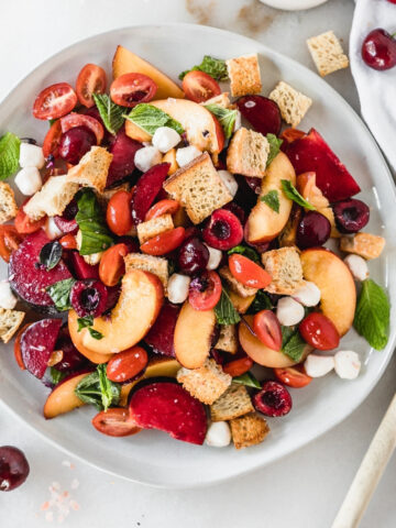 overhead view of stone fruit panzanella salad on a grey plate.