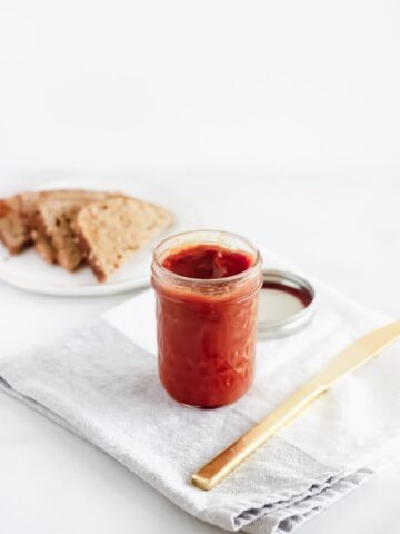 low-sugar wild plum jam in a clear jar on top of a gray and white napkin with a gold butter knife beside it.