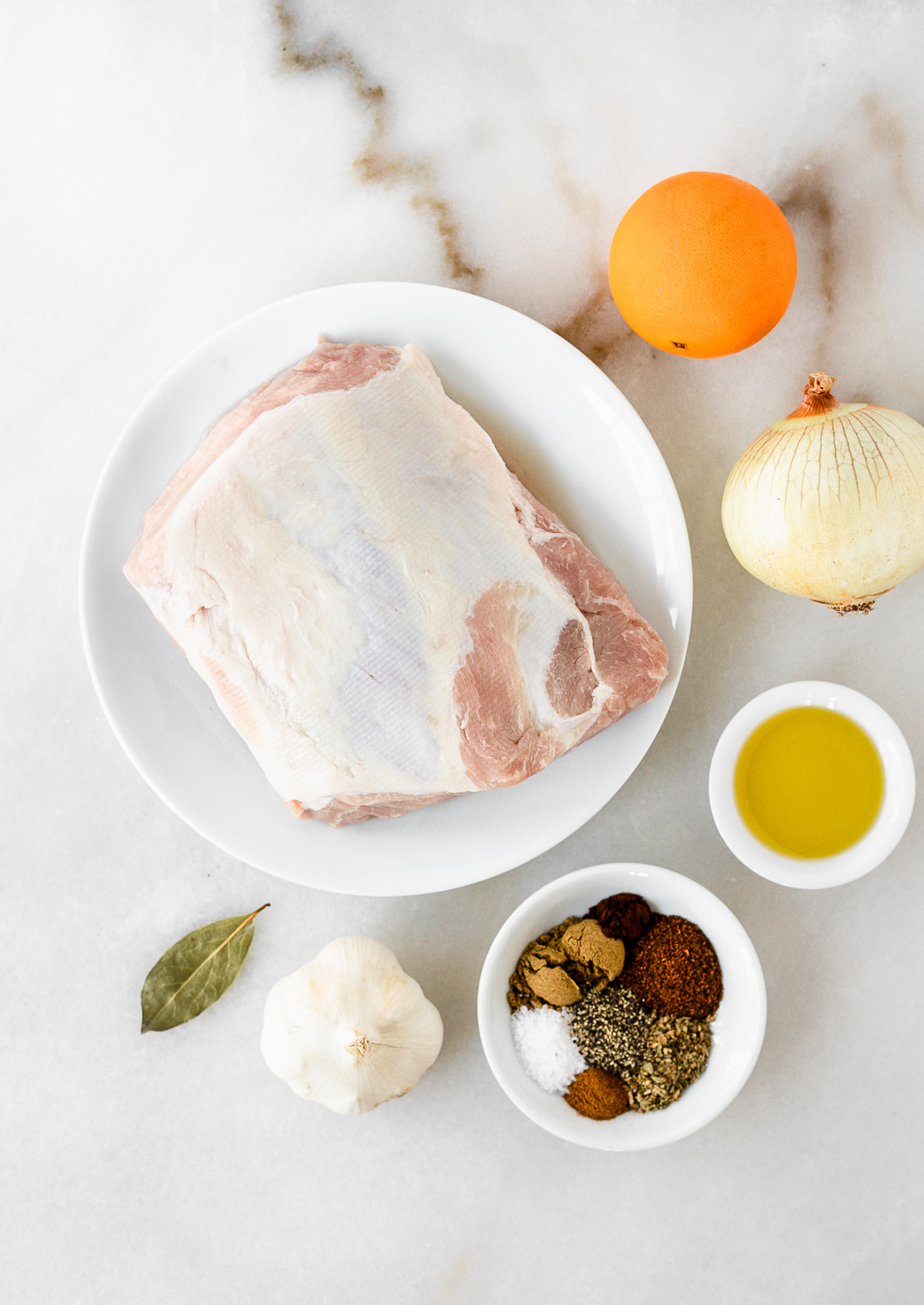 overhead view of ingredients needed to make healthy slow cooker carnitas on a white marble background.