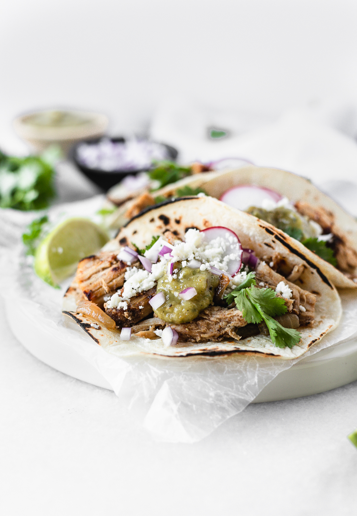 carnitas taco with red onion, cotija, cilntro, radish and green salsa on a plate with a lime wedge.