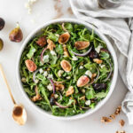 overhead view of fig arugula salad with a gold spoon of balsamic dressing beside it.