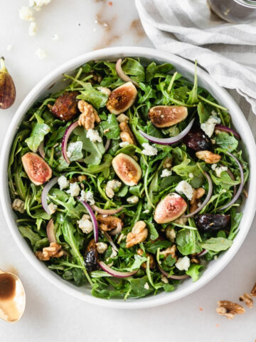 overhead view of fig arugula salad with a gold spoon of balsamic dressing beside it.