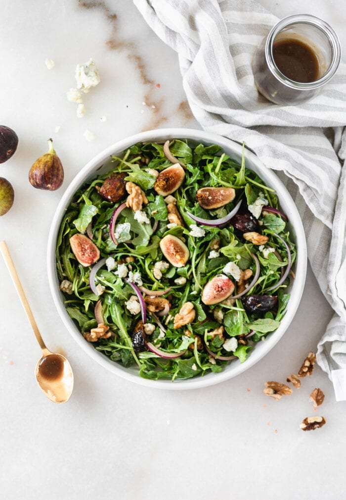 overhead view of fig arugula salad with a gold spoon of balsamic dressing beside it.