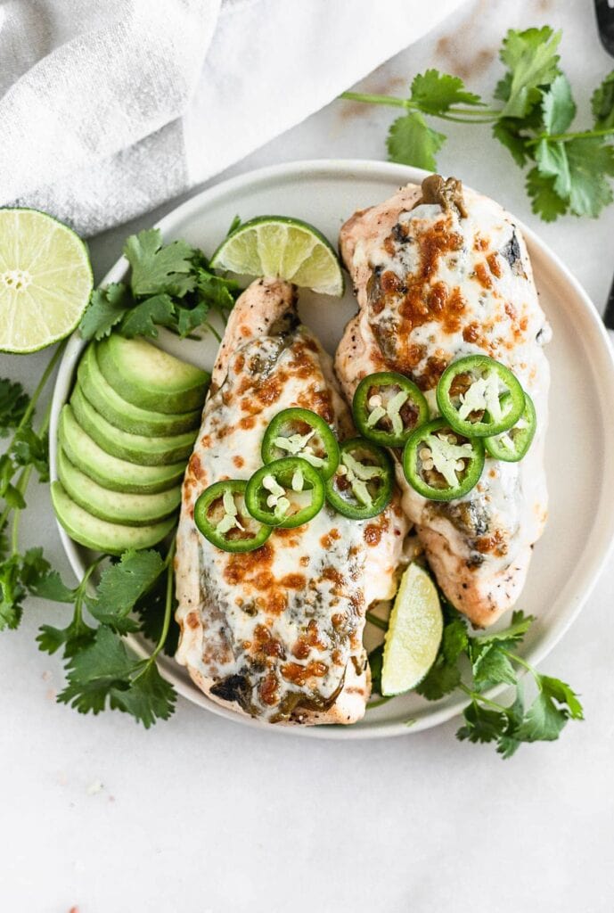 Grilled green chile chicken on a plate with avocado, jalapeños, cilantro, and lime.