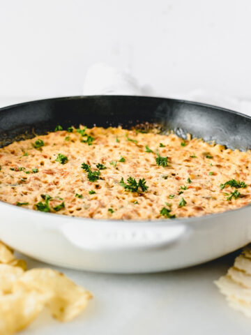 healthier red pepper hot crab dip in a white skillet with chips and crackers around it.