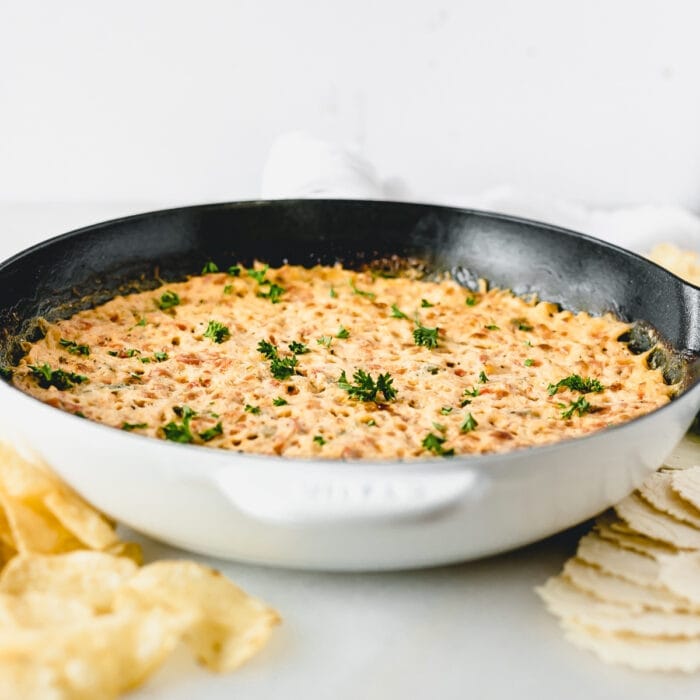 healthier red pepper hot crab dip in a white skillet with chips and crackers around it.