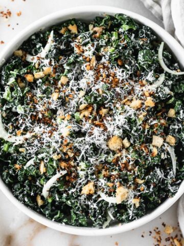 overhead view of kale caesar salad with crouton crumbs and finely shaved parmesan in a white bowl.