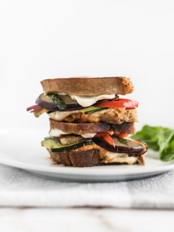 mediterranean veggie hummus grilled cheese cut in half and stacked on each other on a white plate.
