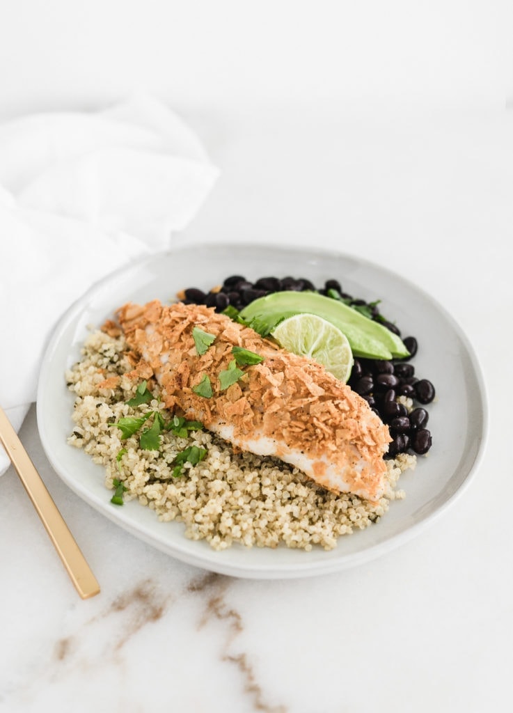 healthy tortilla crusted tilapia in a bowl with quinoa, black beans, and avocado.