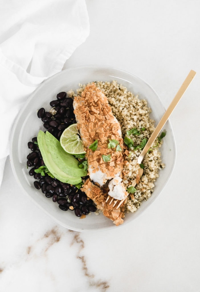 healthy tortilla crusted tilapia on a plate with quinoa, black beans, and avocado.