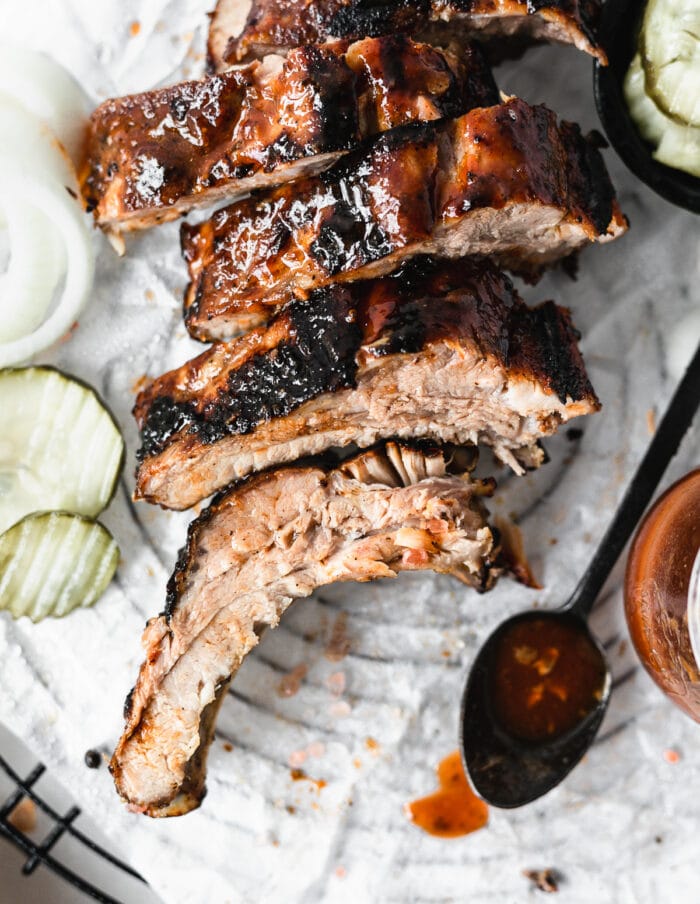 closeup overhead view of sliced bbq ribs on a parchment lined rack with a spoon of bbq sauce.