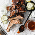 overhead view of sliced bbq ribs on a parchment lined rack with a spoon of bbq sauce.