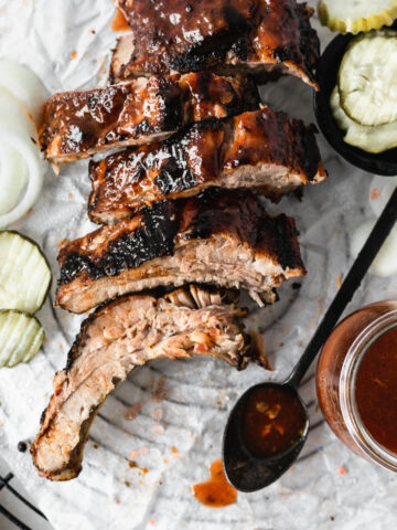 overhead view of sliced bbq ribs on a parchment lined rack with a spoon of bbq sauce.