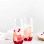 sparkling pear and pomegranate sangria in clear glasses with a white napkin behind it.