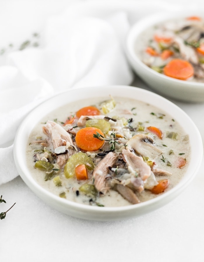 white bowl of healthy turkey and wild rice soup with another bowl of soup in the background.