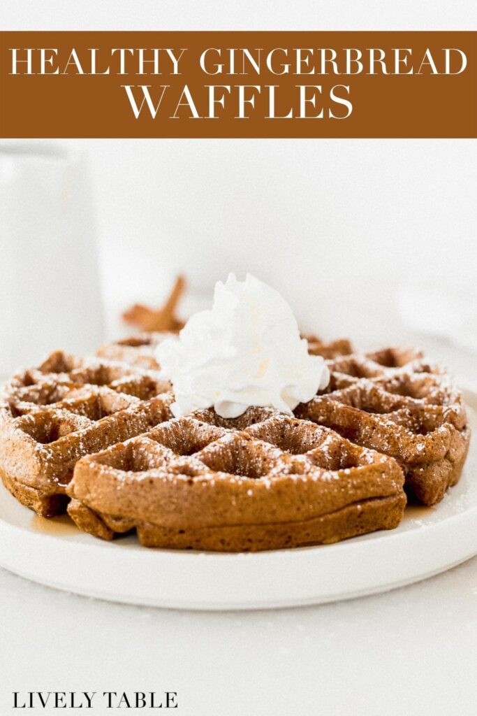gingerbread waffles topped with powdered sugar and whipped cream on a white plate with text overlay.