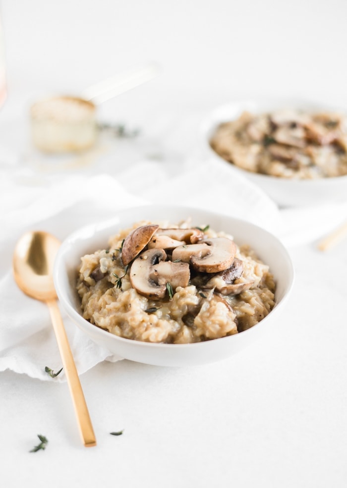healthy mushroom risotto in a white bowl with a gold spoon.