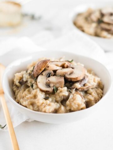 brown rice mushroom risotto in a white bowl with a gold spoon beside it.
