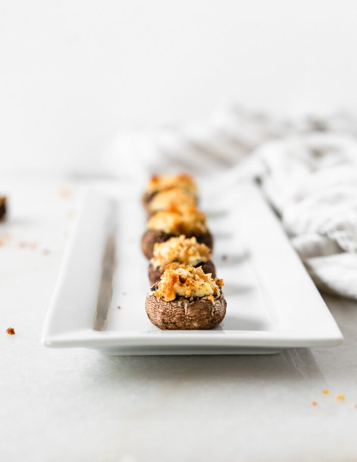 boursin stuffed mushrooms lined up on a white serving platter.