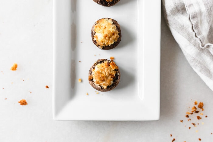 overhead view of boursin stuffed mushrooms on a white serving platter with bread crumbs scattered around.