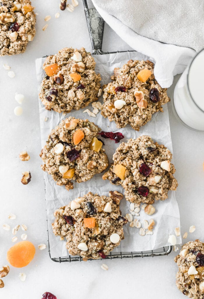 overhead view of fall harvest oatmeal cookies on a cooling rack with cranberries, apricots, walnuts and oats scattered around.
