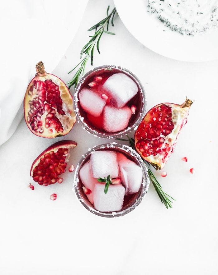 overhead view of two pomegranate ginger smash cocktails surrounded by rosemary and pomegranate pieces.