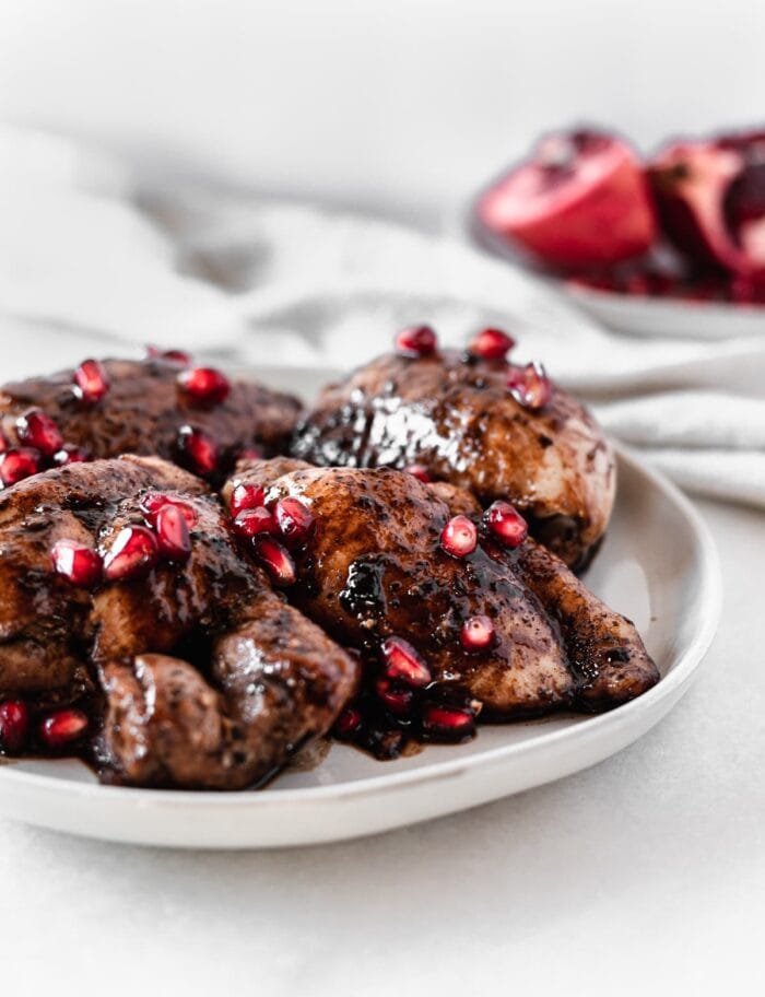 pomegranate balsamic chicken thighs toped with pomegranate arils on a grey plate.