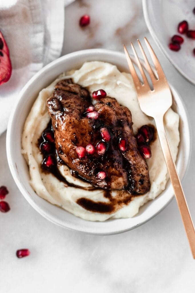 overhead view of pomegranate balsamic chicken in a bowl with mashed potatoes sprinkled with pomegranate arils with a gold fork beside it.