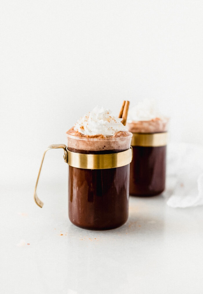 glass mug of tequila spiked mexican hot chocolate topped with whipped cream and a cinnamon stick.