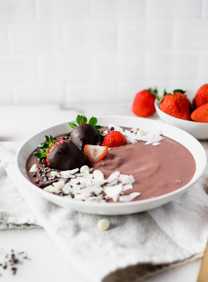 chocolate strawberry smoothie bowl in a white bowl with chocolate covered strawberries and coconut shavings on top.