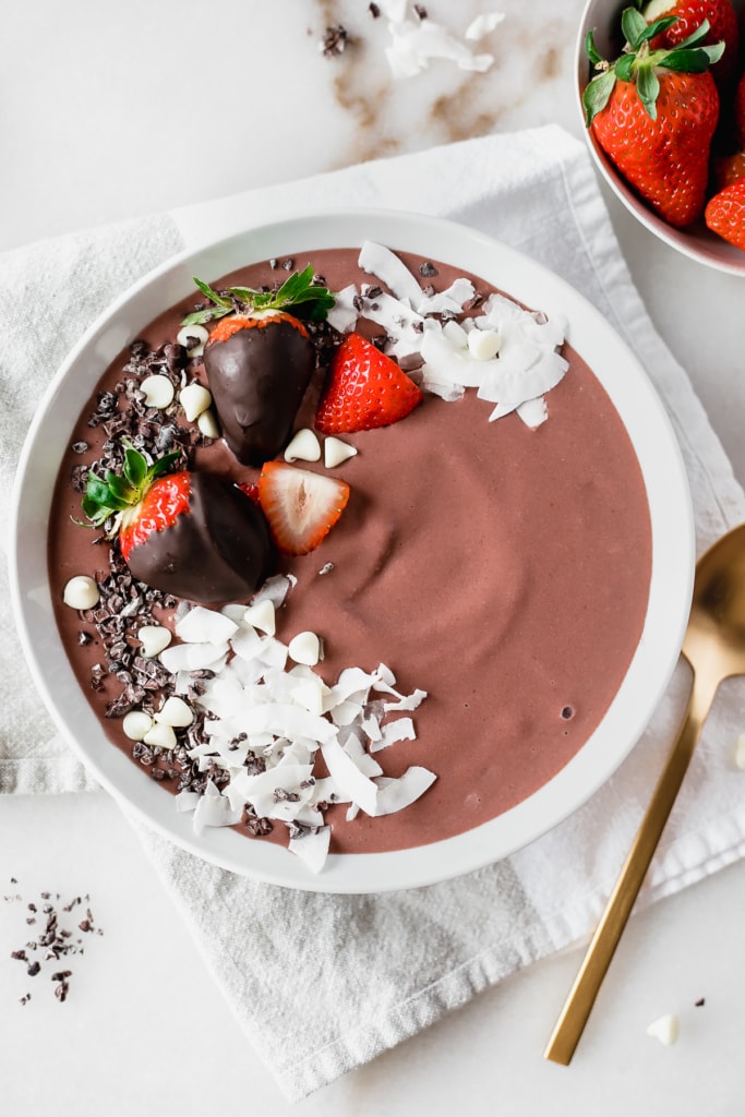 overhead view of chocolate strawberry smoothie bowl in a white bowl with chocolate covered strawberries and coconut shavings on top.