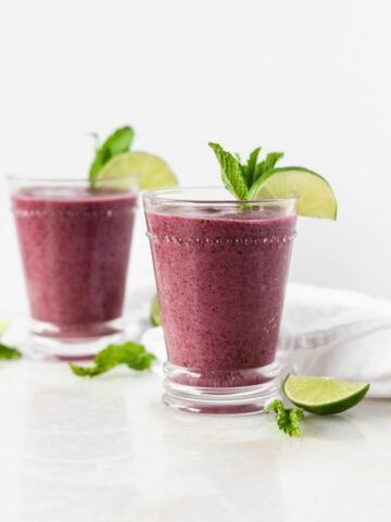 blueberry mojito smoothie in a glass topped with a lime wedge and mint leaves with another smoothie in the background.